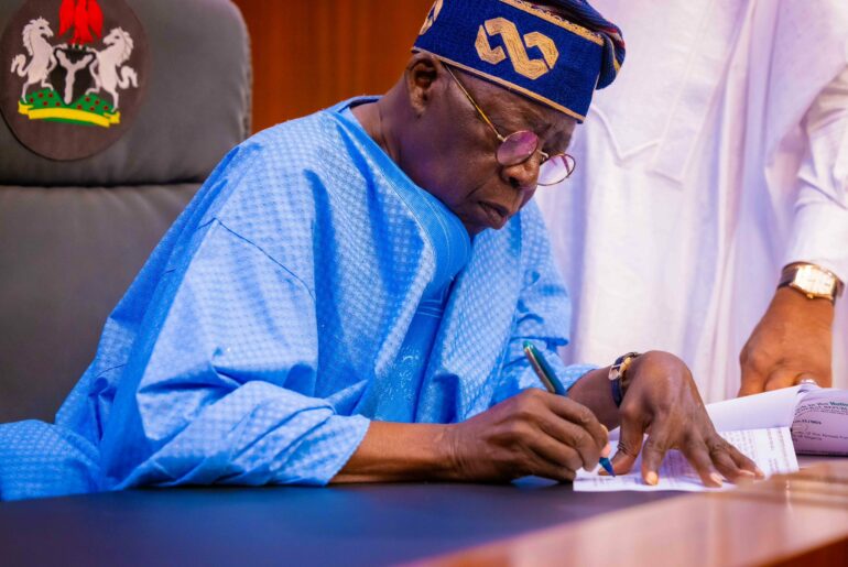 President Bola Ahmed Tinubu sitting at a microphone